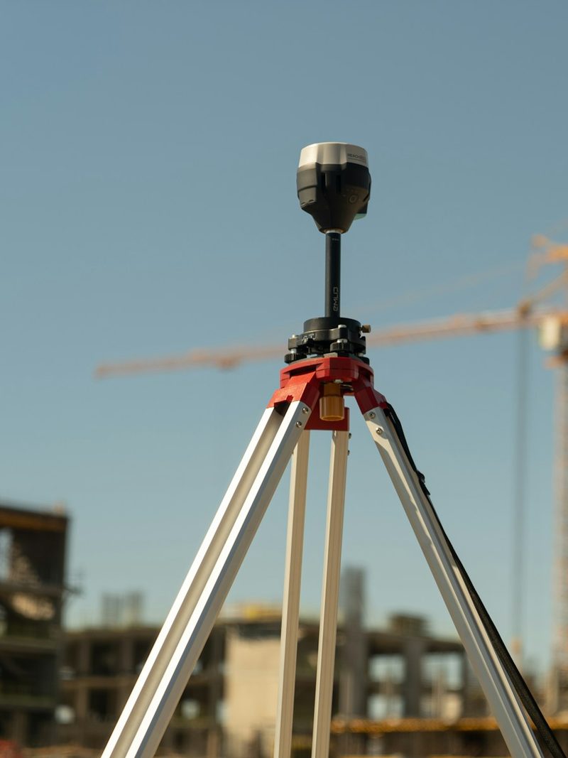 Vermessungsgerät auf einem Stativ vor einer Baustelle mit Kränen